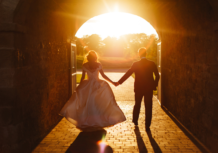 Bride and groom walking towards sunset holding hands